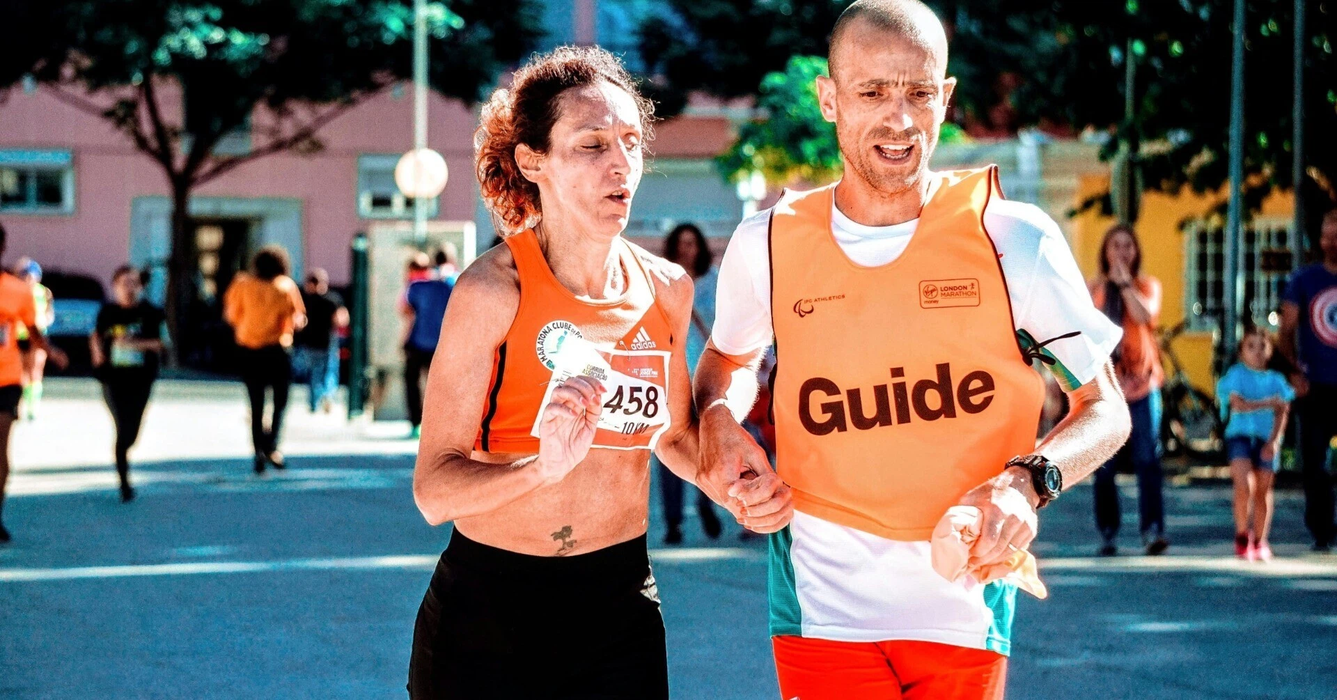 A visually impaired male runner and his guide runner running side-by-side, firmly holding a tether as they move together toward the same goal.