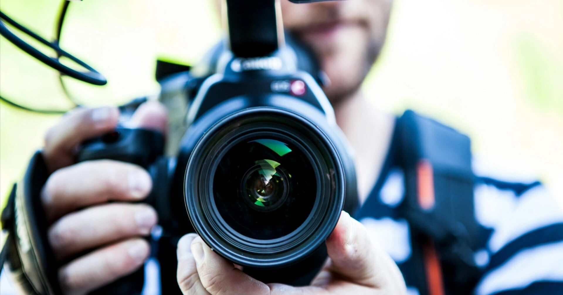A person holding a professional camera with the lens pointed directly at the viewer, symbolizing the intense scrutiny a brand faces during a crisis.