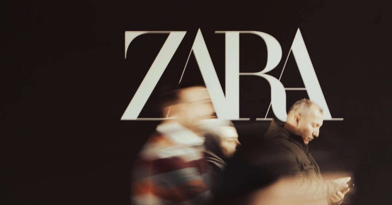 A middle-aged man in a business suit walks quickly past a ZARA storefront, while a blurred figure of a younger man is visible in the background.