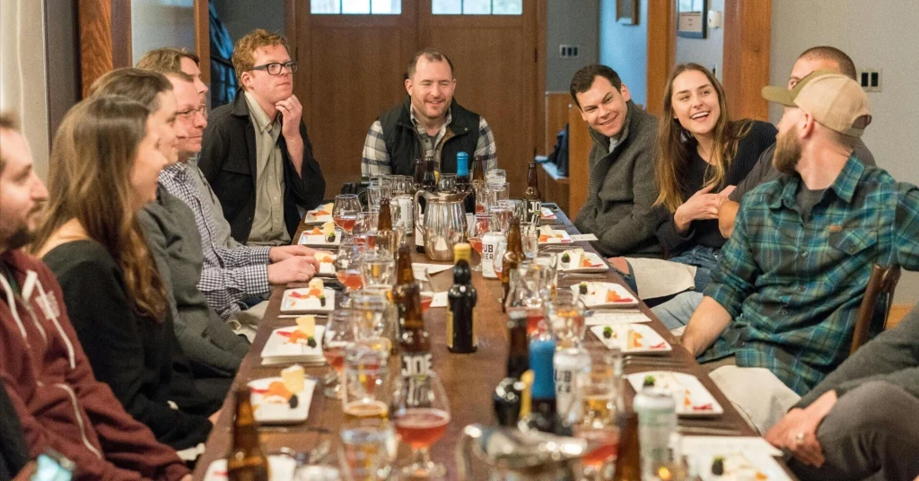 A group of men and women enjoying dinner and beer at a long table in a casual restaurant