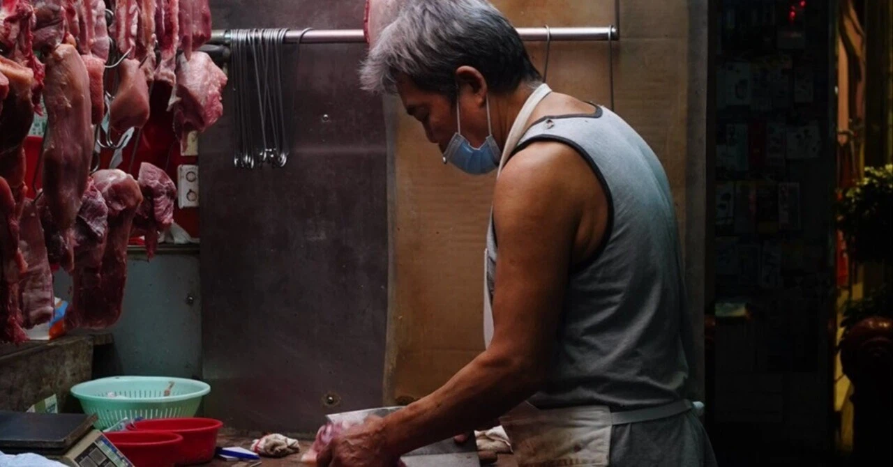 香港のローカル精肉店で、マスクをした精肉店の店主が中華包丁で肉をさばいている様子