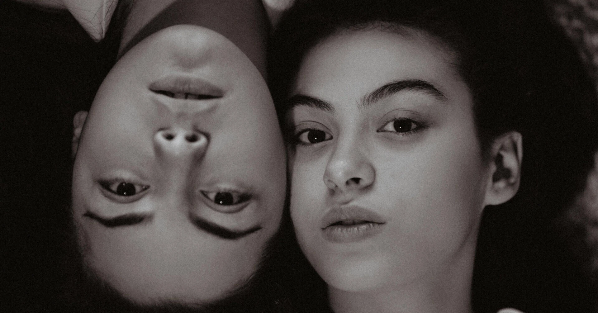 Close-up of the faces of two young people lying in opposite directions. A black and white photo with strong, impressive gazes.