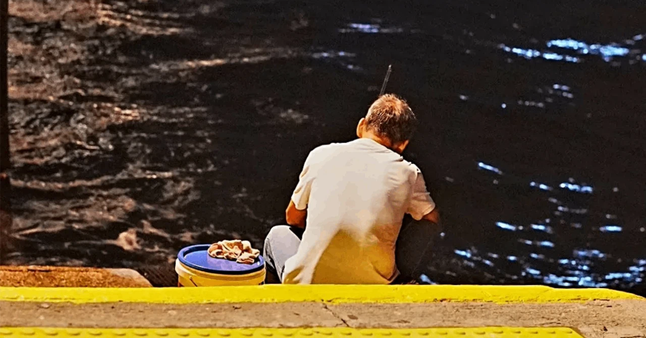 夕暮れのオレンジ色の光に照らされる、香港の小さな埠頭で夜釣りを楽しむ人のシルエット