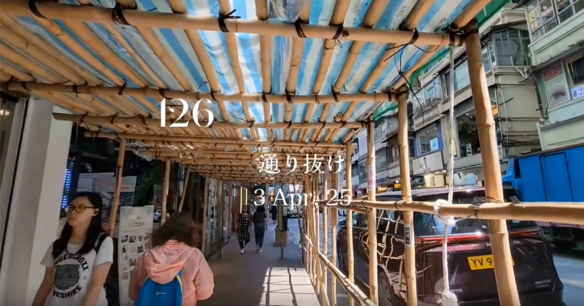 香港の街中にある、竹の足場（竹スキャフォールディング）で覆われた歩道を通り抜ける人々