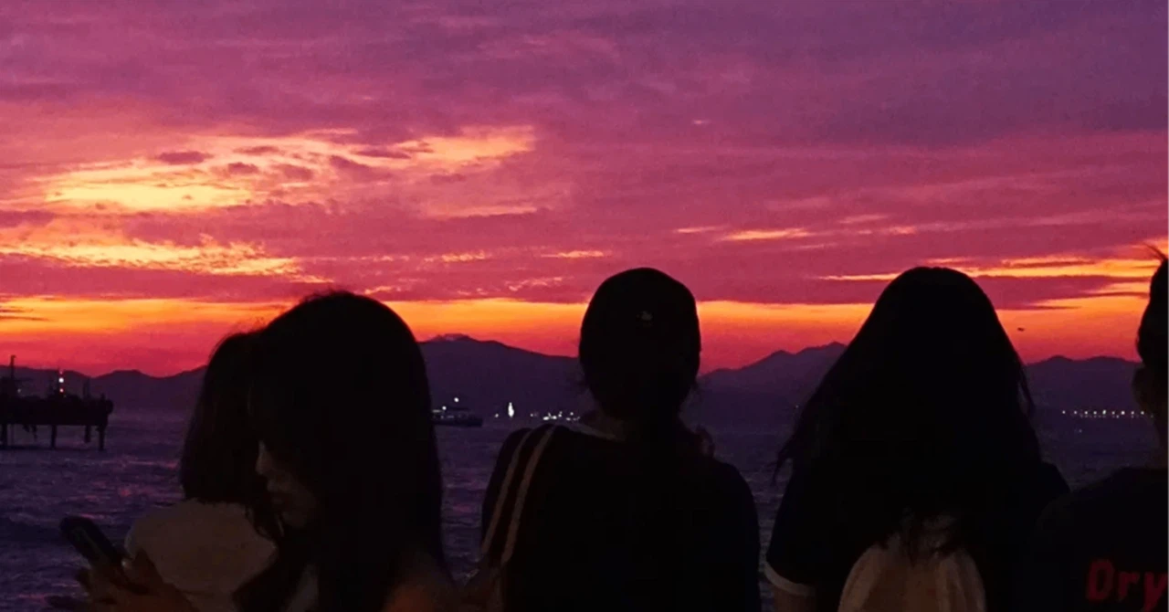 香港の海辺でマジックアワーの夕焼けと海の景色を背景に佇む人々のシルエット。空は紫とピンクに染まっている。
