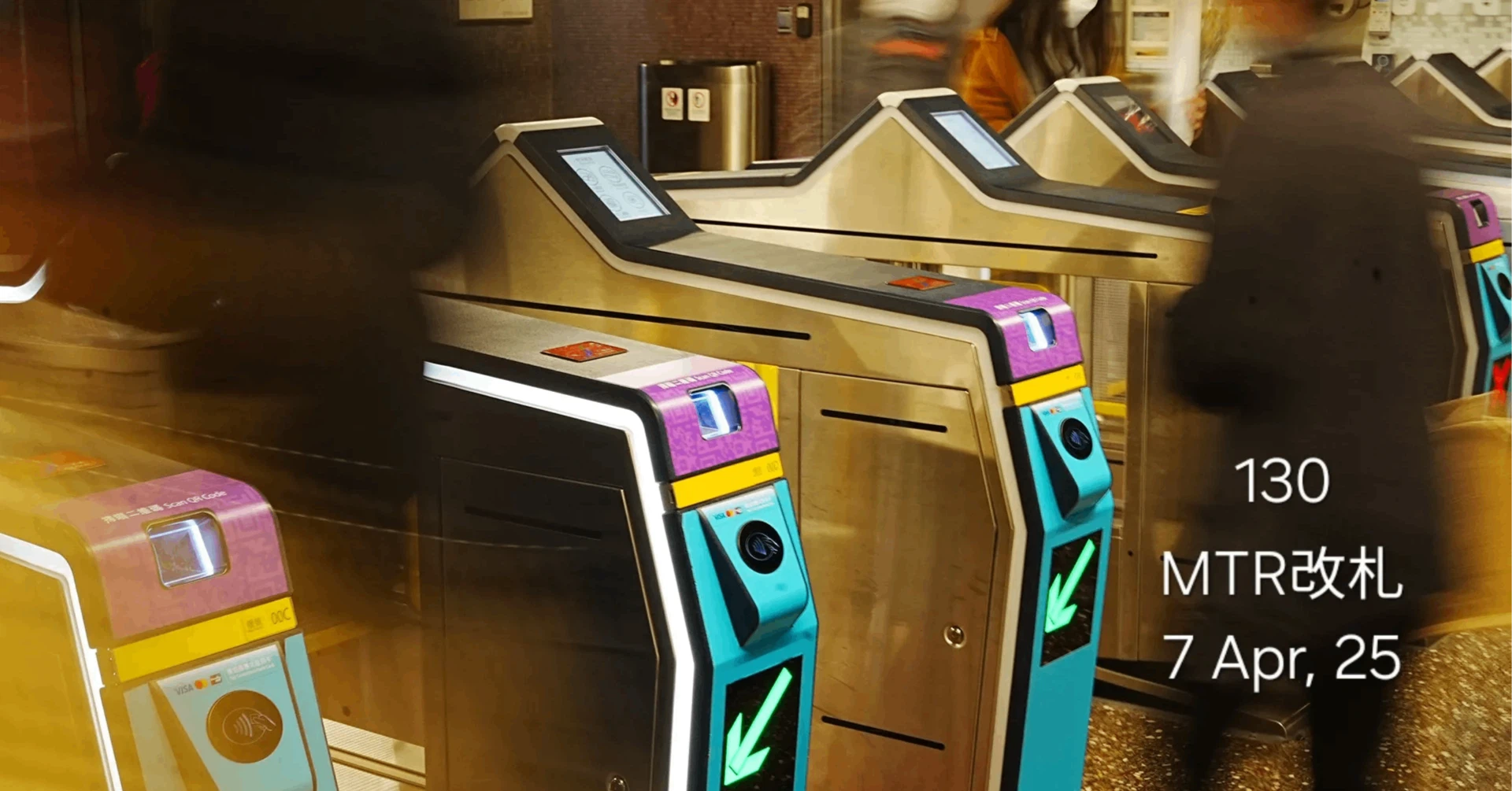 香港MTRの駅に設置された、クレジットカードのタッチ決済やQRコードに対応した新型改札機と、行き交う人々の残像
