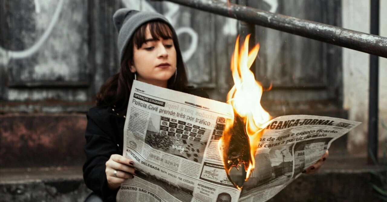 A young woman reading a burning newspaper, symbolizing fake news and the unreliability of information