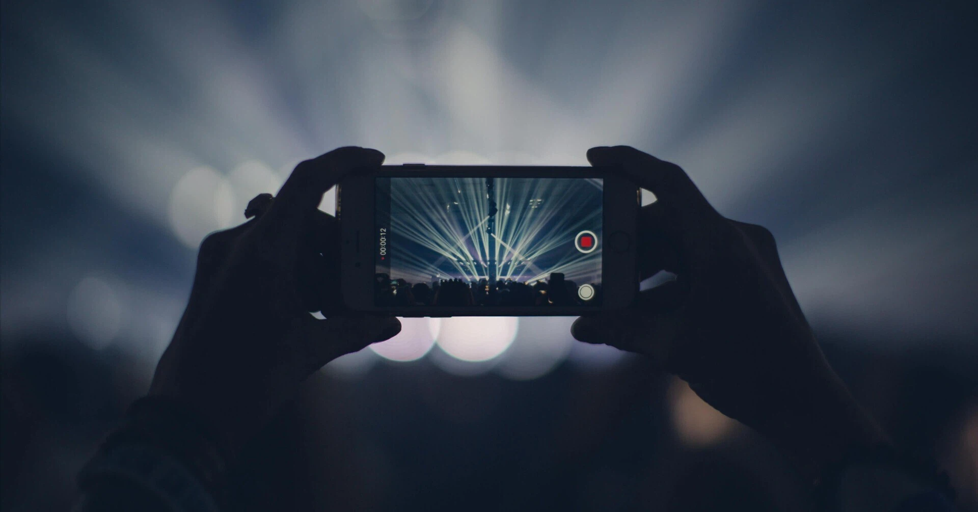 The hands of an audience member holding up a smartphone to record a video amidst the excitement of a live concert