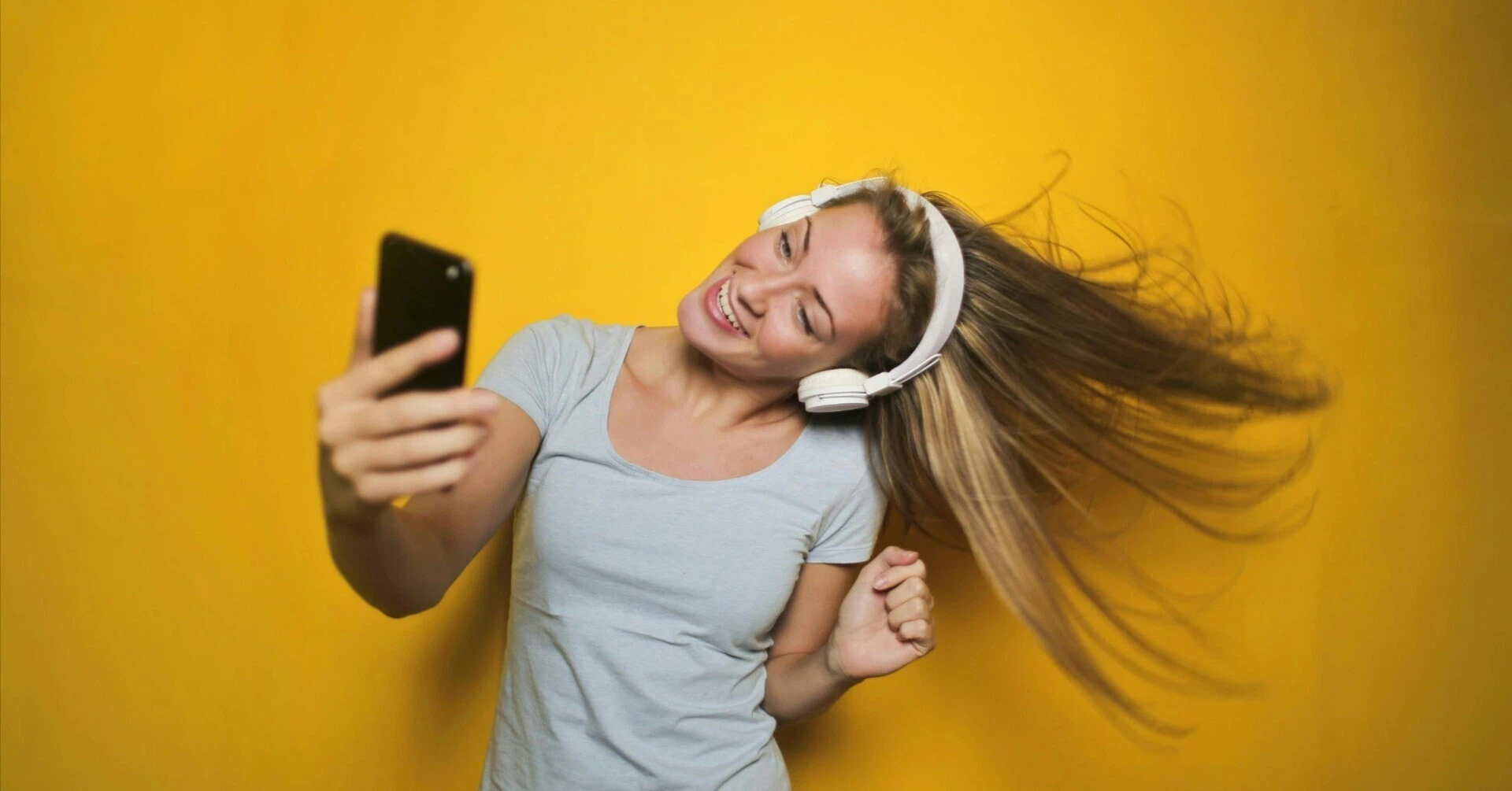 A woman dancing energetically while listening to music on headphones and looking at her smartphone