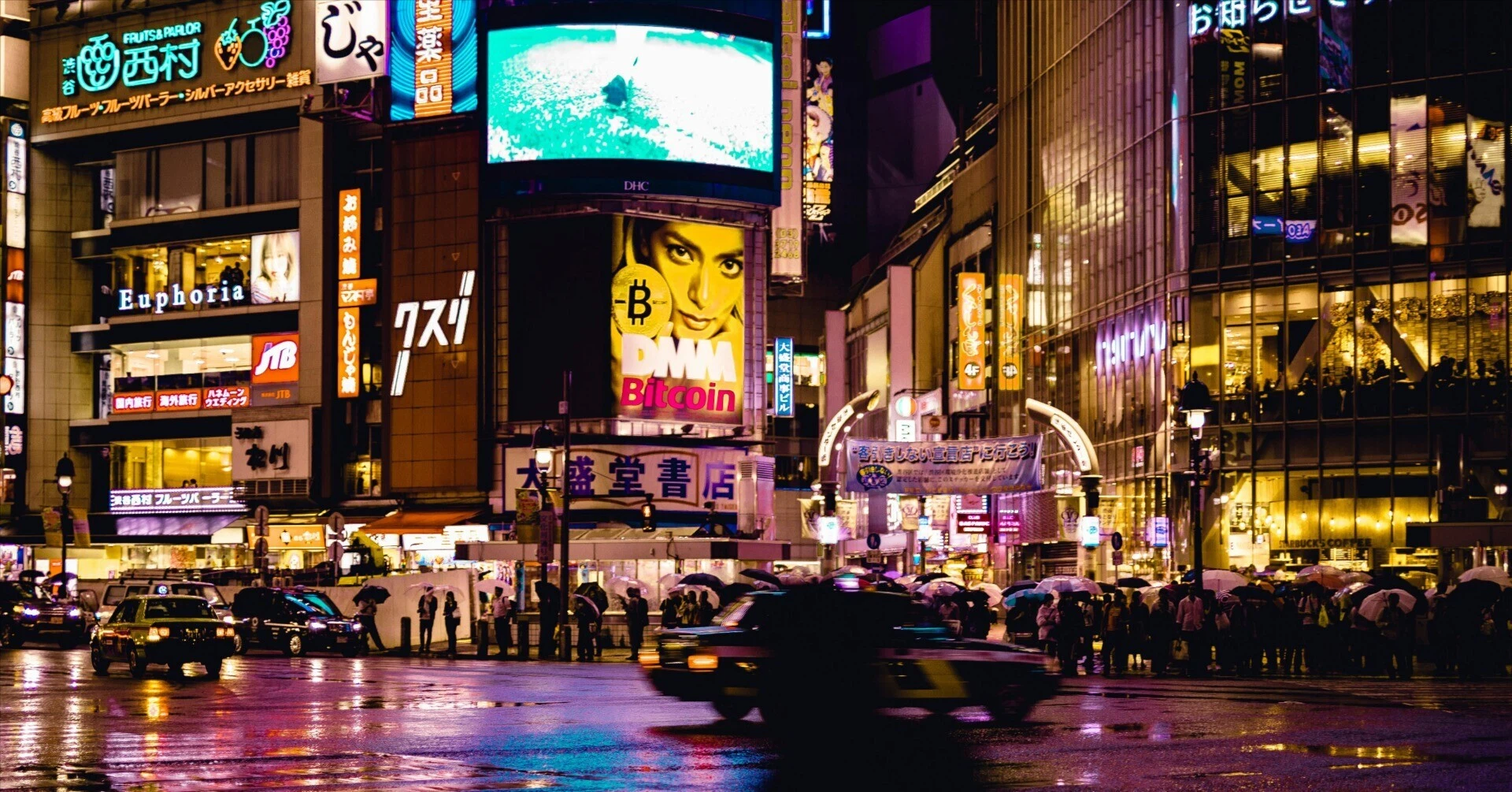 People walking through the Shibuya crossing on a rainy night illuminated by bright neon signs