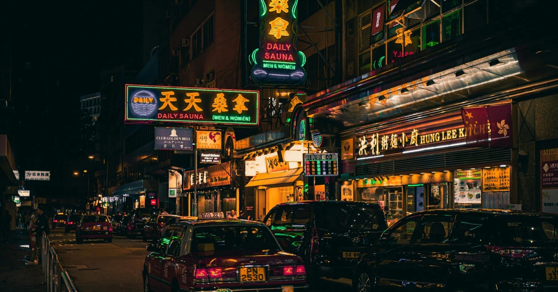 ネオンサインが輝く夜の香港の通りと、客待ちをして並ぶタクシーの列