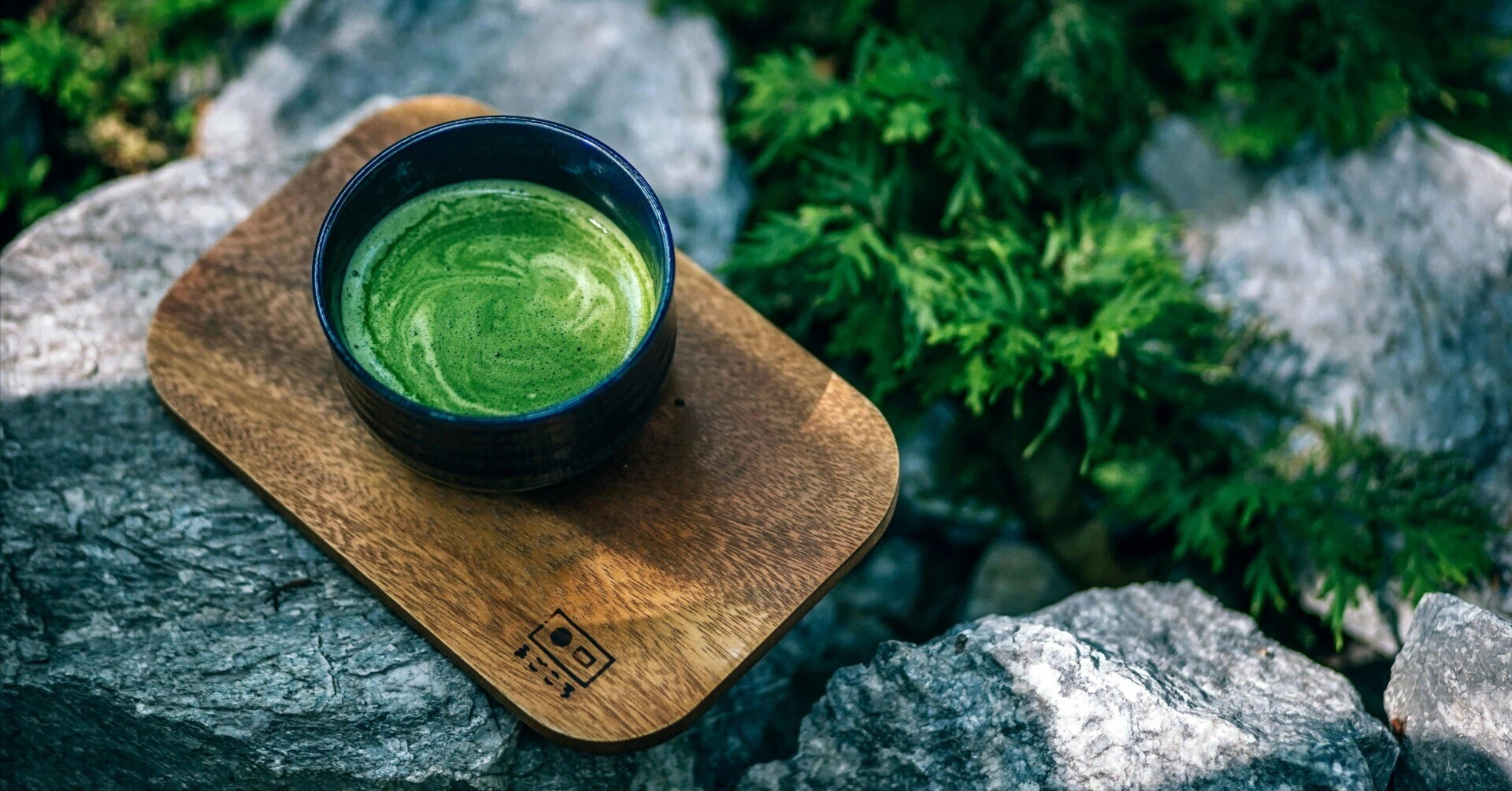 石の上に置かれた木の板に乗った、美しい緑色に点てられた抹茶